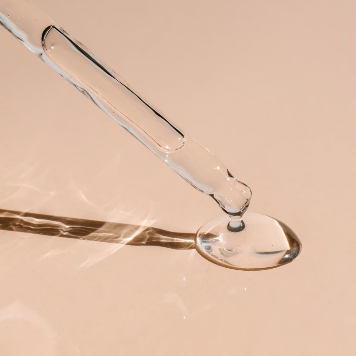 Close-up of a glass dropper with liquid on a beige background