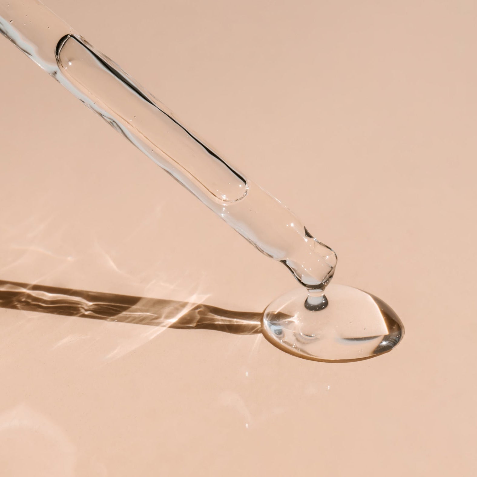 Close-up of a glass dropper with liquid on a beige background